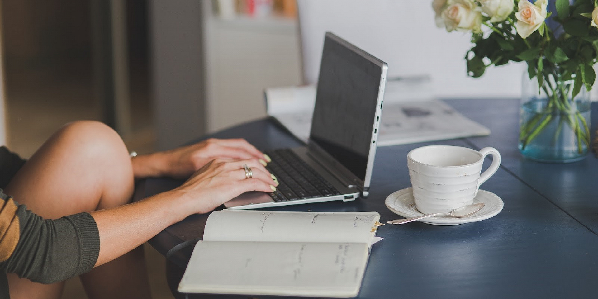 Mains de femme travaillant sur un ordinateur portable avec un cahier et un café