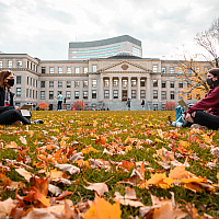 Two students study together in the field in front of the Tabaret building using their laptops