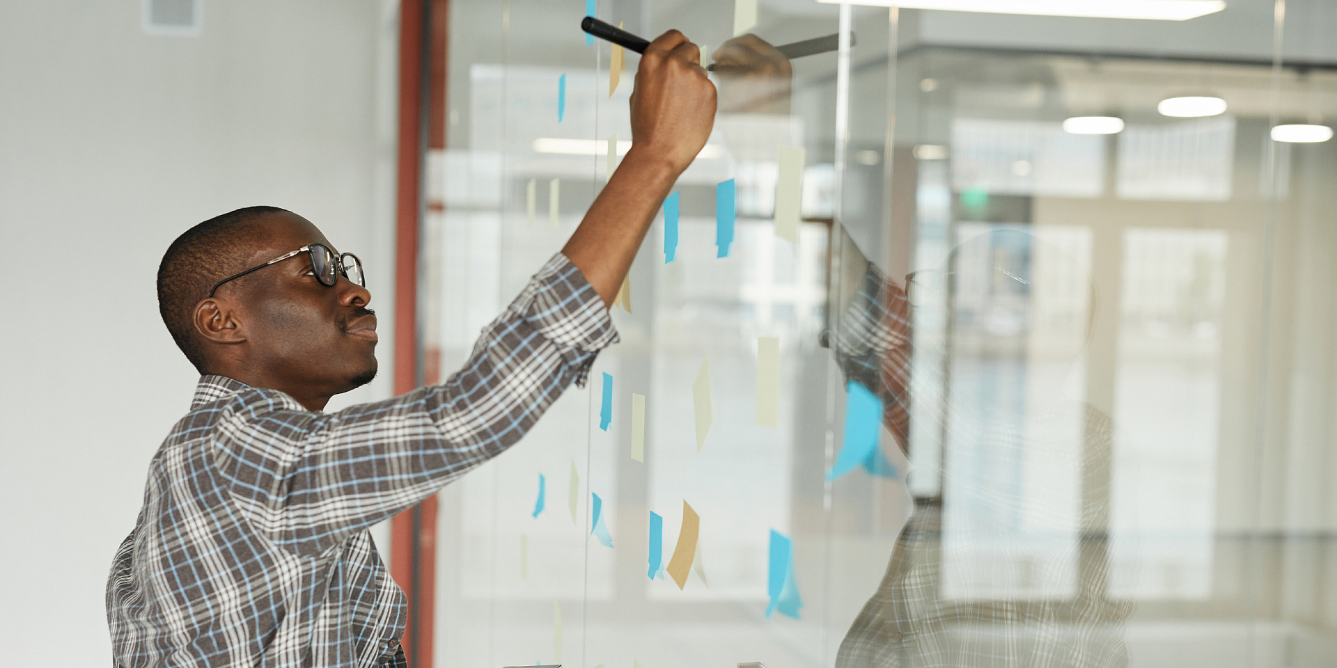 Business man writing on a post-it on glass wall