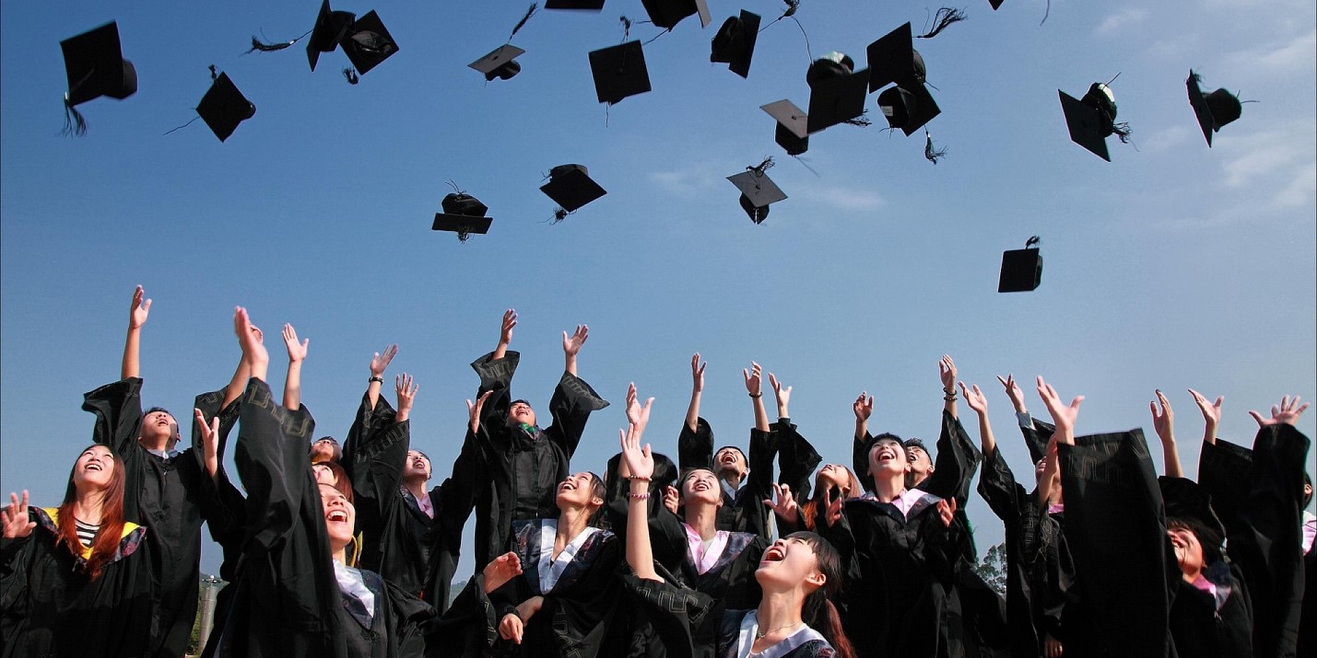 Students throwing their graduate caps into the air on a summer day