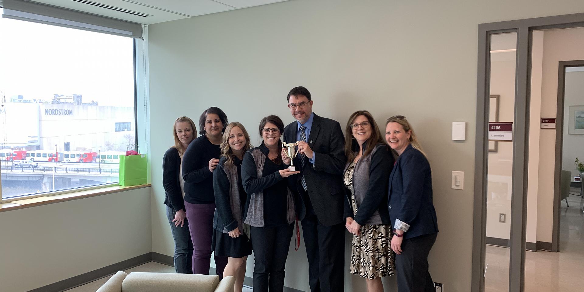 Telfer employees with the Dean hold a trophy, smiling.