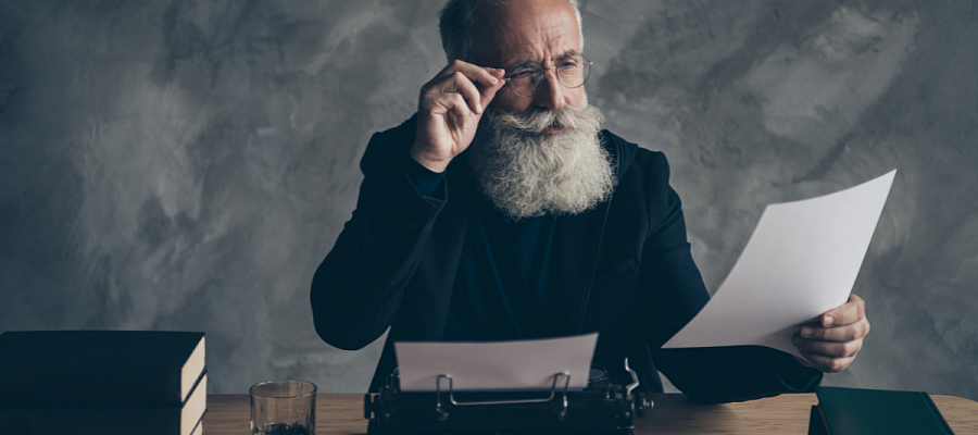 man with a typewriter scrutinizing a sheet of paper