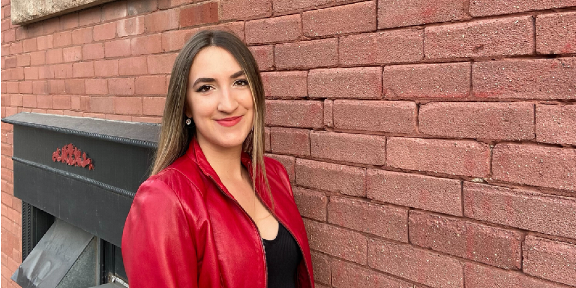 Jessica Roe with a red coat in front of a brick wall.