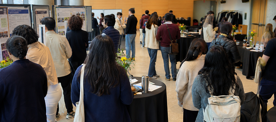 Students and community members gather in the Camille Villeneuve Room for a poster showcase and networking event, viewing project displays and engaging in conversations around standing tables.