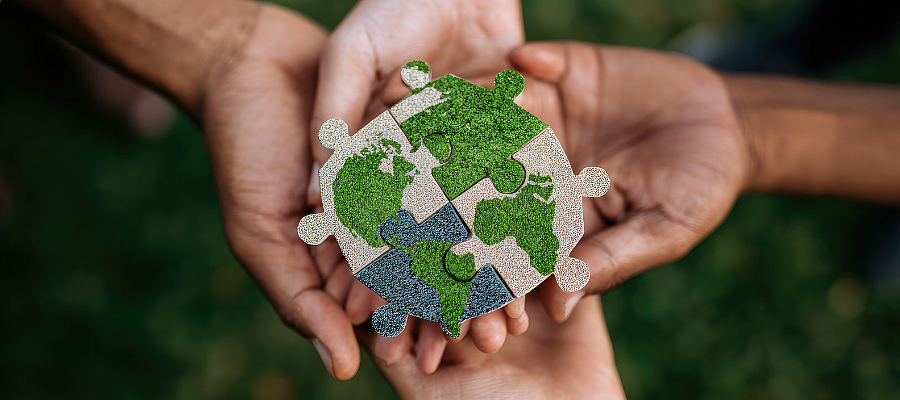 Mains de trois personnes tenant un globe en forme de puzzle, symbolisant la collaboration, la durabilité et la responsabilité partagée envers la planète.