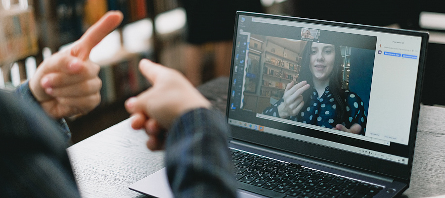 Image over the should of a person talking (useing their hands) to a person on the screen in an online meeting.