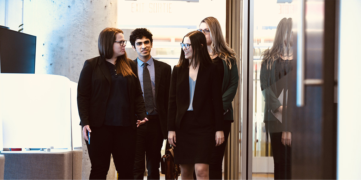 Four well-dressed students walk down a hallway