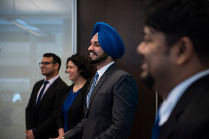 A diverse group of four students dressed in business attire, standing and smiling.